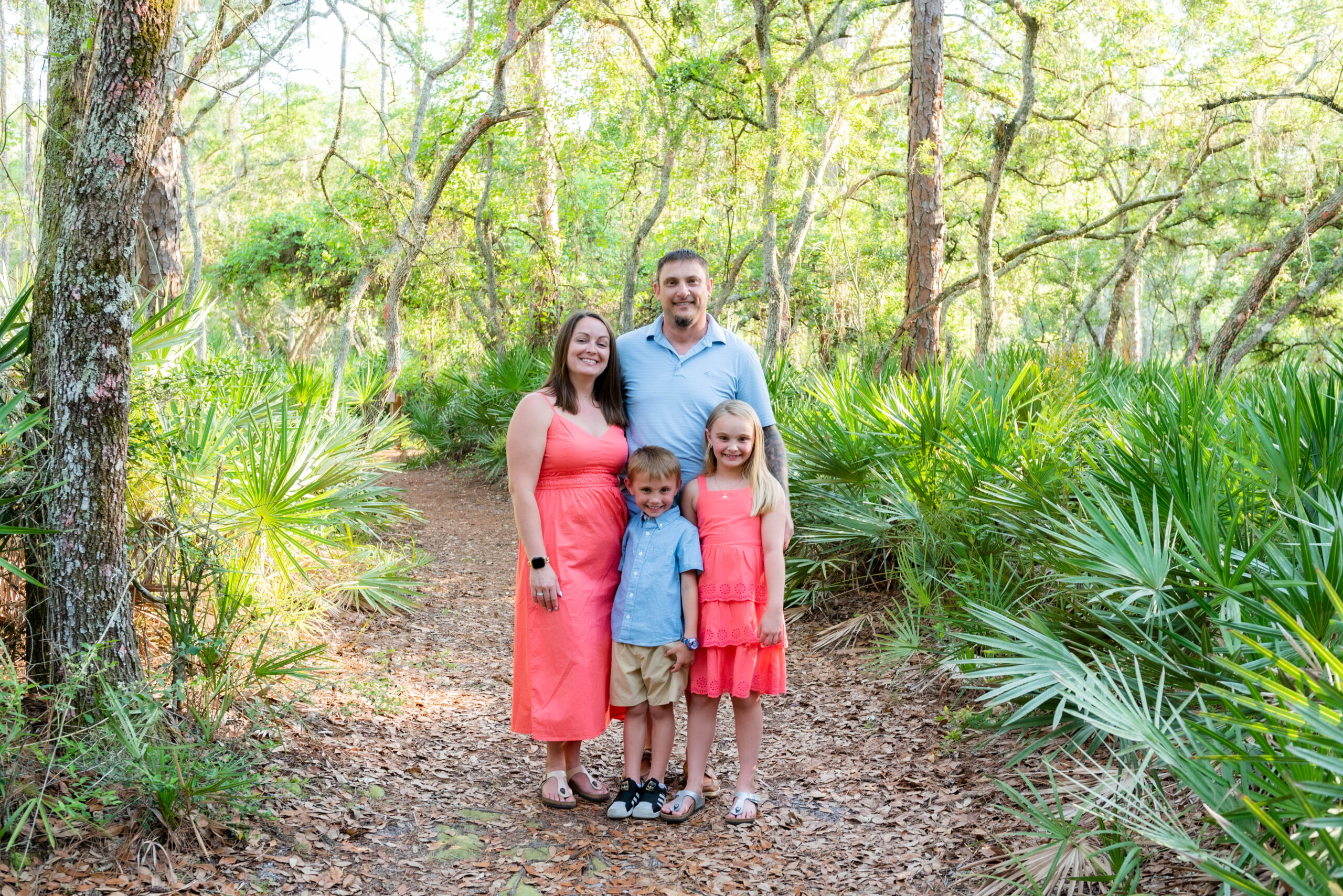 Family portrait in a forest with parents and two children smiling.